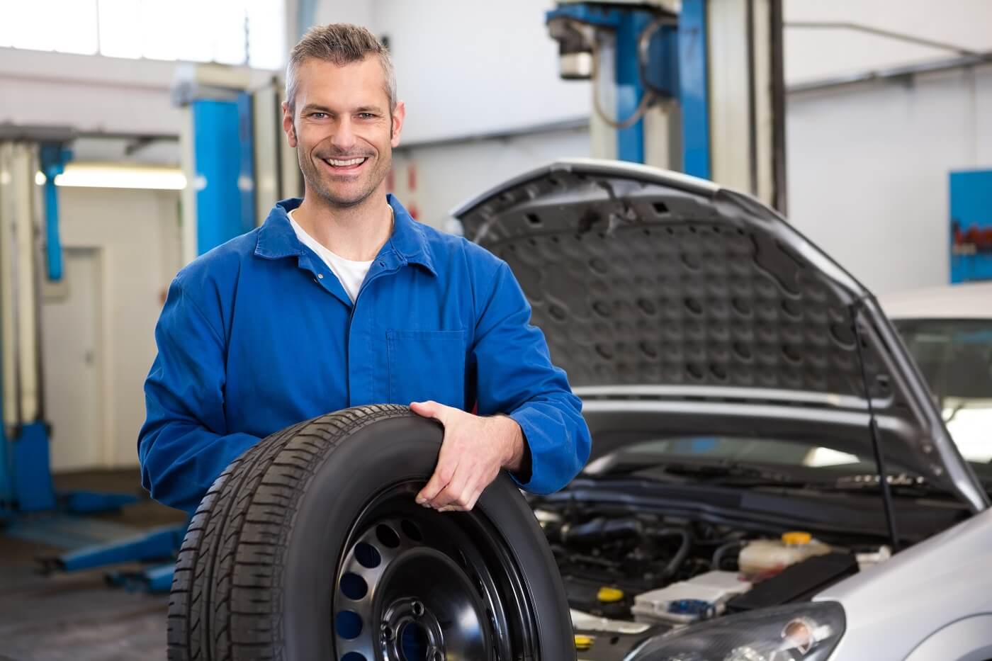 Service technician holding a tire in front of a car with its hood open