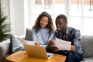Couple sitting on a couch in front of their laptop and looking at car paperwork